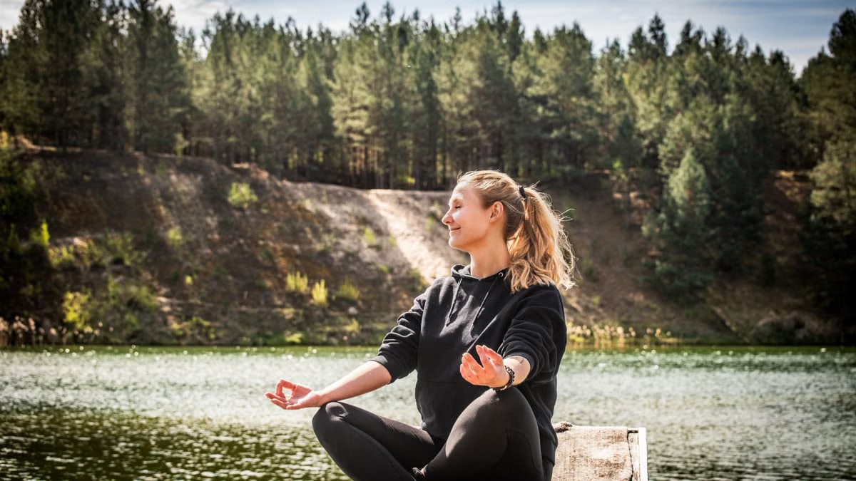 Serene moment of a woman practicing meditation near a forest lake in Lithuania.